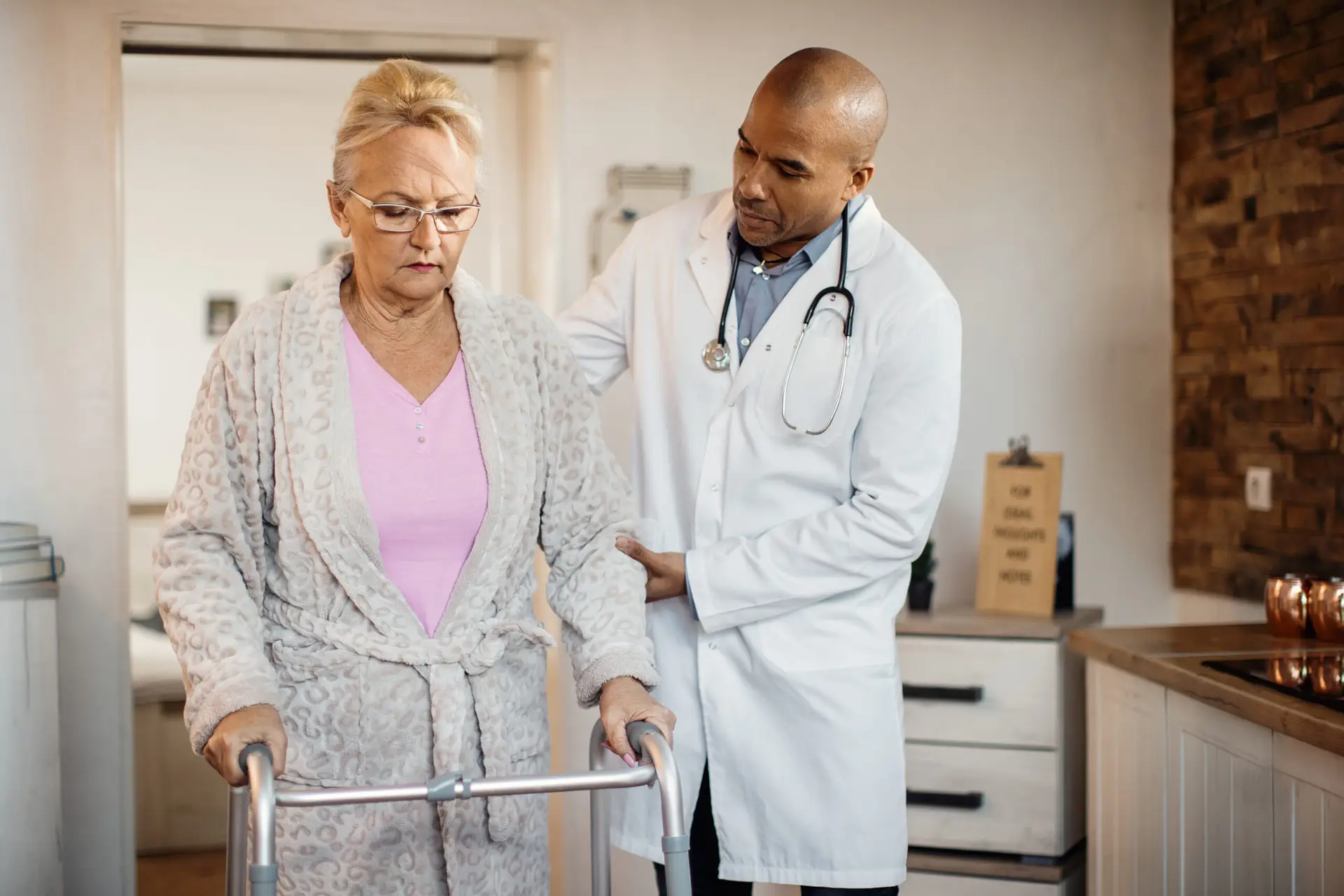 Senior woman using a walker with help of African American doctor at nursing home.
